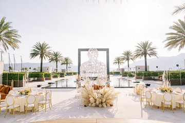 Festive tables stand on the outdoor terrace by the pool near a wicker wire sculpture