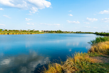Summer sunny day. Panorama with a lake in the countryside. On the opposite bank of the lake there is a village	