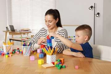 Cute boy and teacher with colorful cubes at desk in school