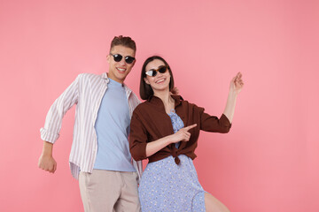 Happy couple in stylish clothes dancing on pink background