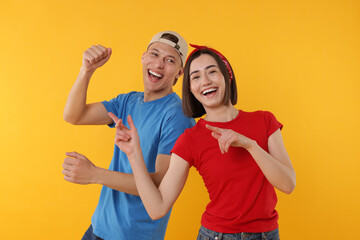 Obraz premium Happy couple in stylish clothes dancing on yellow background