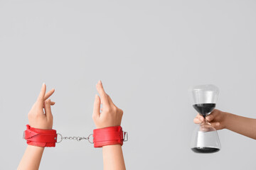 Female hands with hourglass and handcuffs on grey background