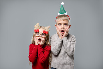 Funny children in Christmas accessories on grey background