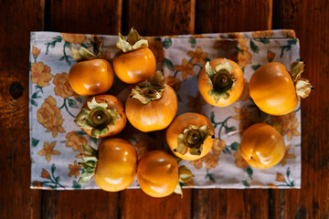 Ripe persimmons are laid out on a colorful napkin on a wooden table. Top view