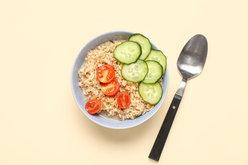 Tasty oatmeal with tomato and cucumber in bowl on beige background