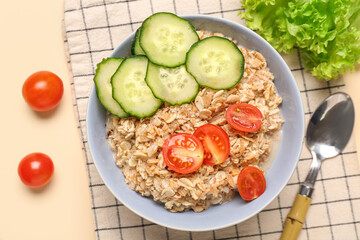 Bowl with tasty oatmeal and vegetables on beige background