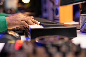 Musician producer hitting notes on piano electronic keyboard, editing his music in post production with mixing console. Artist composing songs with sounds from synthesizer midi controller. Close up,