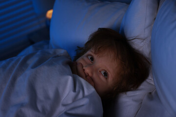 Scared boy hiding under duvet in bed at night