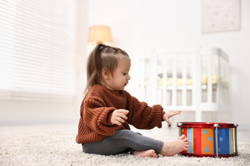 Cute little girl playing with toy drum on floor at home