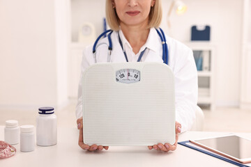 Weight loss. Nutritionist with scales at table in clinic, closeup