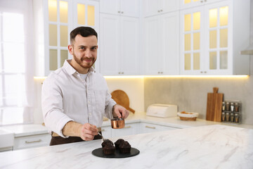 Confectioner adding chocolate sauce to muffins at white marble table in kitchen, space for text