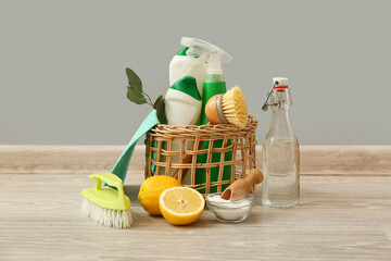 Wicker basket with natural cleaning supplies on wooden floor against grey wall