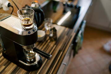 Glass of coffee stands on a carob coffee machine preparing coffee in a cup
