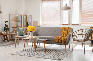 Interior of living room with grey sofa, carpet, coffee tables and vase of narcissus flowers
