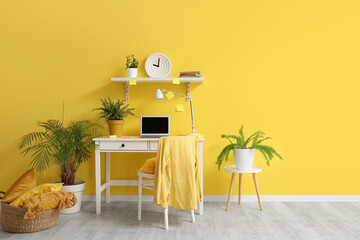 Beautiful room with workplace, laptop, chair and clock on yellow wall