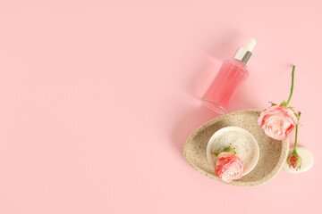 Bottle of cosmetic oil, roses, bowl and stone tray on pink background