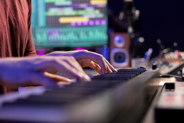 Music producer playing tunes on electronic midi controller, composing songs to use with mixing and mastering techniques. Singer plays electronic piano notes to create soundtracks. Close up.