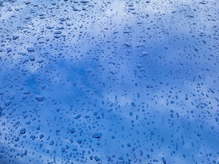 Raindrops and reflections on the blue metal surface of the hood on a summer day