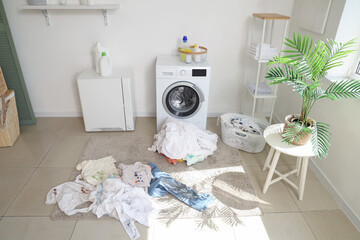 Interior of light laundry room with modern washing machine and pile of dirty clothes on floor