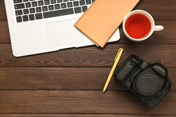 Composition with photo camera, modern laptop, stationery and cup of tea on dark wooden background
