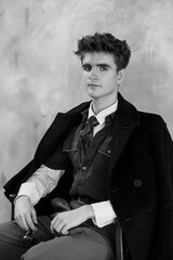 Fototapeta premium Black and white portrait of a young man in formal attire, wearing a coat, vest, tie, and shirt, with a thoughtful expression and textured backdrop