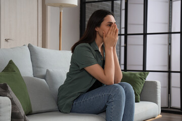 Depressed young woman sitting on sofa at home