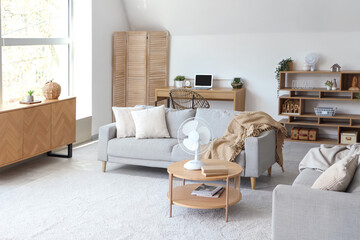 Interior of light living room with modern electric fan on coffee table