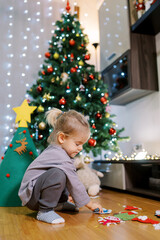 Little girl sorts out toys for a felt Christmas tree while squatting