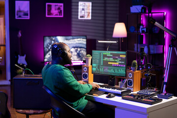 Audio producer playing piano electronic synthesizer to create a new tune, adjusting volume levels on old recordings. Music engineer recording sounds, plays tracks on midi controller.