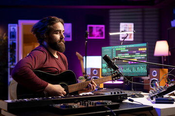Musical composer singing tunes on acoustic instrument, working in his personal home studio to...