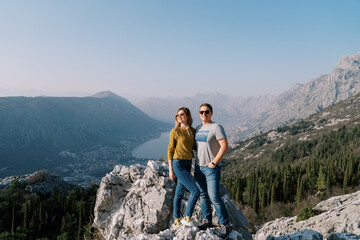 Smiling man hugs woman on a rock above the Bay of Kotor. Montenegro