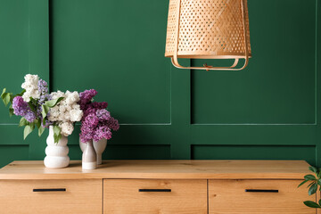 Stylish wooden cabinet and vase with flowers near green wall in room