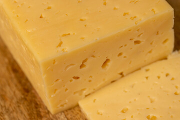 hard cheese with holes for cooking, pieces of sliced cheese on a board, close up