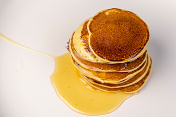 pancakes and bee honey on a white bowl, a tower of small milk pancakes on a ceramic bowl with honey, close up
