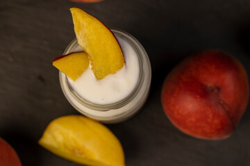 yogurt and peaches cut into pieces on black slate, fermented milk product with peach flavor with the addition of pieces of peach