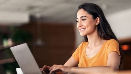 Smiling pretty girl using laptop at cafe, working online, empty space