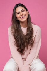 Fototapeta premium Smiling young asian female in pink sweater against pink background