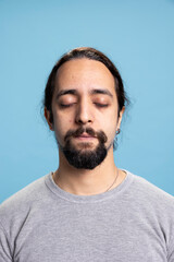 Fototapeta premium Young mindful casual adult doing a Zen meditation session with eyes closed, advertising wellness and concentration for a great balance in life. Male model meditating and relaxing in studio.