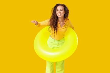 Beautiful young African-American woman with inflatable ring on yellow background