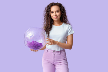 Beautiful young African-American woman with beach ball on lilac background