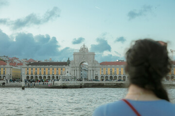 A woman looks across the Tagus River at Lisbon’s iconic Praça do Comércio and Arco da Rua...