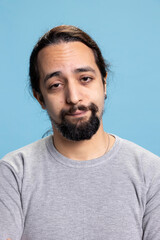 Obraz premium Confident person with a beard and curly hair posing in studio, peaceful authentic masculine guy in a casual wear. Young adult standing against blue background, ambitious man with arms crossed.