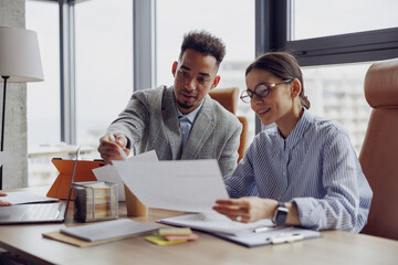 Two professionals discuss essential documents in a modern office to enhance collaboration and...