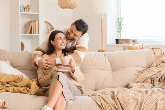 Happy young couple with cup of tea hugging at home on autumn day
