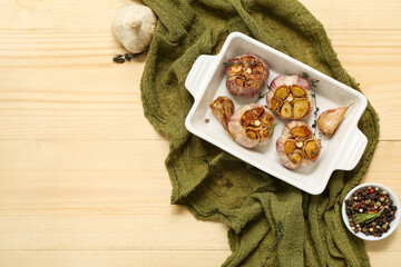 Baking dish with garlic, peppercorns, rosemary and thyme on light wooden background