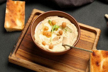 Bowl of delicious hummus with chickpeas, micro green and baked bread on black background
