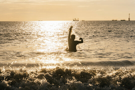 Fisherman casting net at sunset in tranquil sea waters