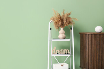 Vase with pampas grass and decor on stepladder near green wall in room
