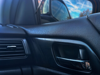 Close-up of sleek black car interior showing textured dashboard, inner door handle, and air vent....