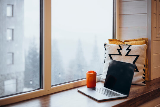 Cozy home office setup with laptop and thermos cup by window